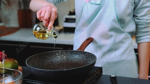 Woman pouring a large amount of vegetable oil into a frying pan. Close-up shot of table. Cooking in the kitchen.