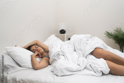 Woman in nightgown sleeps in comfortable position on bed with light pastels in bedroom with potted plant in apartment lady rests getting energy from sleeping