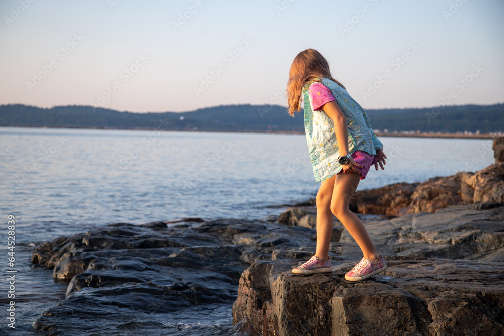 Girl crouching on rock at edge of lake, Lake Superior