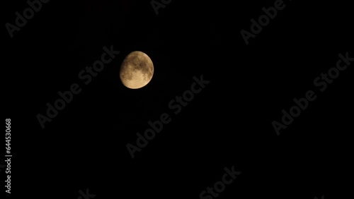 Clear moon with black clouds. 4k footage video. The partly clear moon is setting down. Black clouds float against the backdrop of the yellow moon with craters. Close-up. Natural satellite of Earth