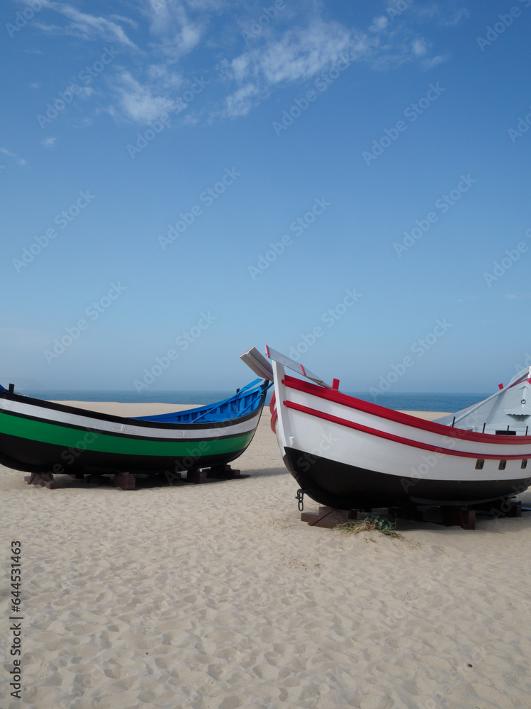 Fototapeta premium sets of two antique fishing boats on the beach of Nazaré, Portugal. Restored painting. nice sunny day with the sea in the background. vertical photo