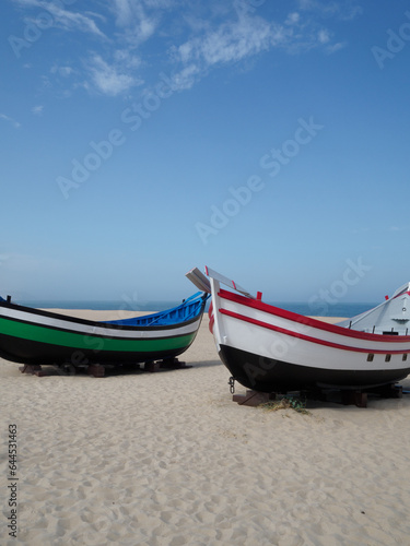 sets of two antique fishing boats on the beach of Nazaré, Portugal. Restored painting. nice sunny day with the sea in the background. vertical photo