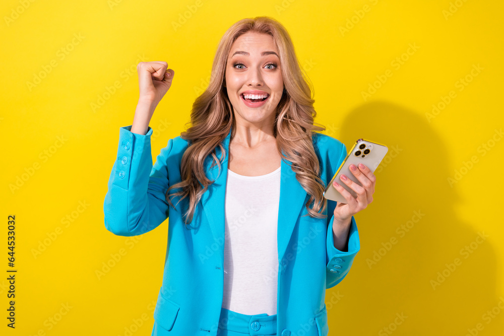 Photo of delighted pretty person hold smart phone raise fist success achievement isolated on yellow color background Photo of delighted pretty person hold smart phone raise fist success achievement isolated on yellow color background