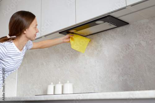 Housework and cleaning service concept. Woman hand cleaning range hood in the kitchen with a rag or cloth.