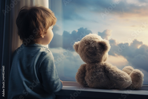 A little boy and his teddy bear toy admire the sunset. 