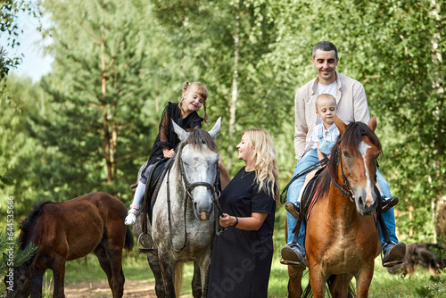 Happy family: father, son, mother and daughter having fun riding horse. Outdoor fun for kids. Evening forest walk.