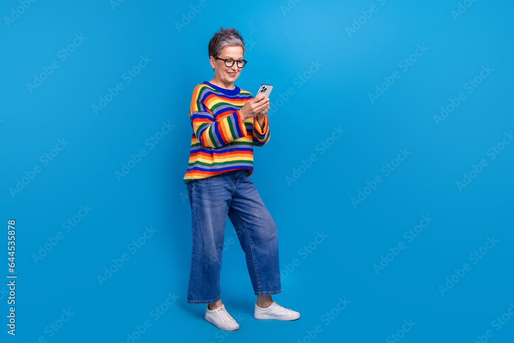 Full size profile photo of nice cheerful lady use smart phone chatting empty space isolated on blue color background Full size profile photo of nice cheerful lady use smart phone chatting empty space isolated on blue color background