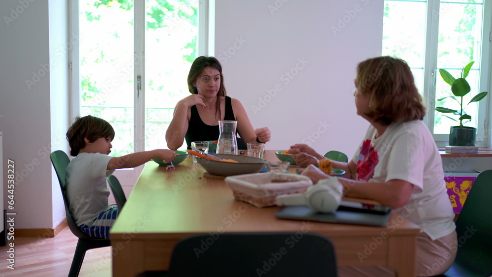 Candid family scene lifestyle at home, casual elderly woman with adult woman and child sitting at lunch table eating meal Candid family scene lifestyle at home, casual elderly woman with adult woman and child sitting at lunch table eating meal