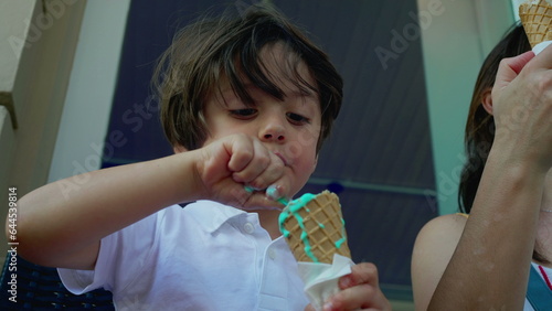 Concentrated small boy savoring colorful blue ice-cream cone at parlor outside during summer day  close-up of a caucasian male child eating sweet dessert