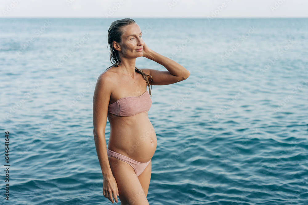 A young pregnant woman stands on the seashore after swimming. A young pregnant woman stands on the seashore after swimming.