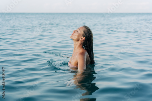 A beautiful woman emerges from the sea water. Blissful woman swimming in the sea in pleasure.