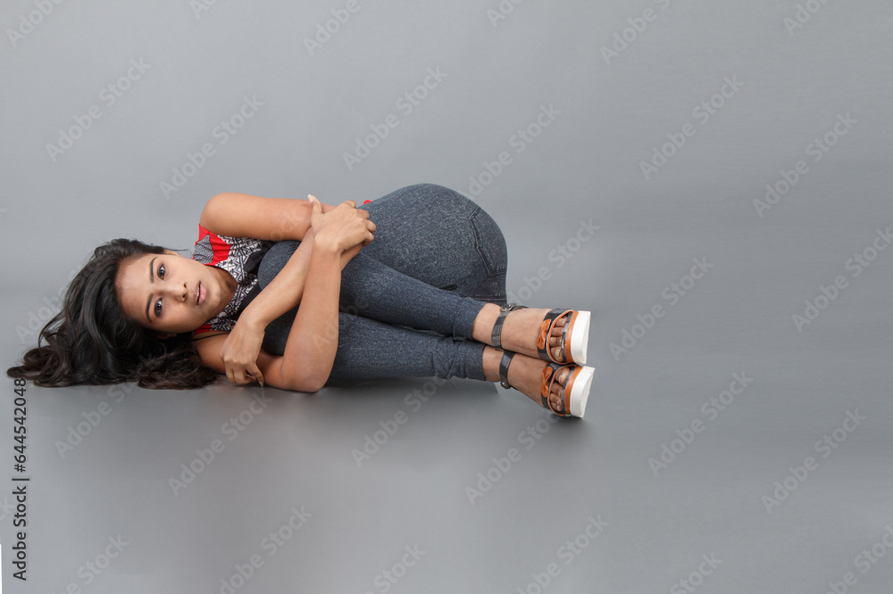 Studio shot of a young, beautiful Indian female model in casual wear wearing red and grey designer top and blue jeans against grey background. Female model. Fashion Portrait. Studio shot of a young, beautiful Indian female model in casual wear wearing red and grey designer top and blue jeans against grey background. Female model. Fashion Portrait.