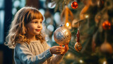 Winter families holidays. Cute small girl hangs a New Year's ball on Christmas tree on blurred interior background. Christmas card. lifestyle, copy space