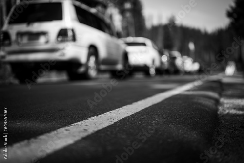 Selective focus on a paved road with a defocused long line of vehicles to enter a national park in the background