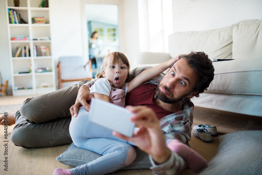 Young father taking a selfie on a smartphone with his daughter in the living room at home Young father taking a selfie on a smartphone with his daughter in the living room at home