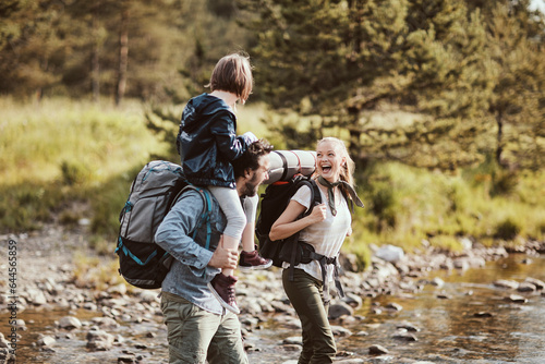 Young family crossing a creek while hiking in the forest and mountains