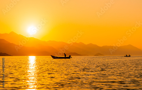 Silhouette of a fishing boat with a fisherman fishing in the orange sunset of Shkoder Lake in Shiroka. Albania