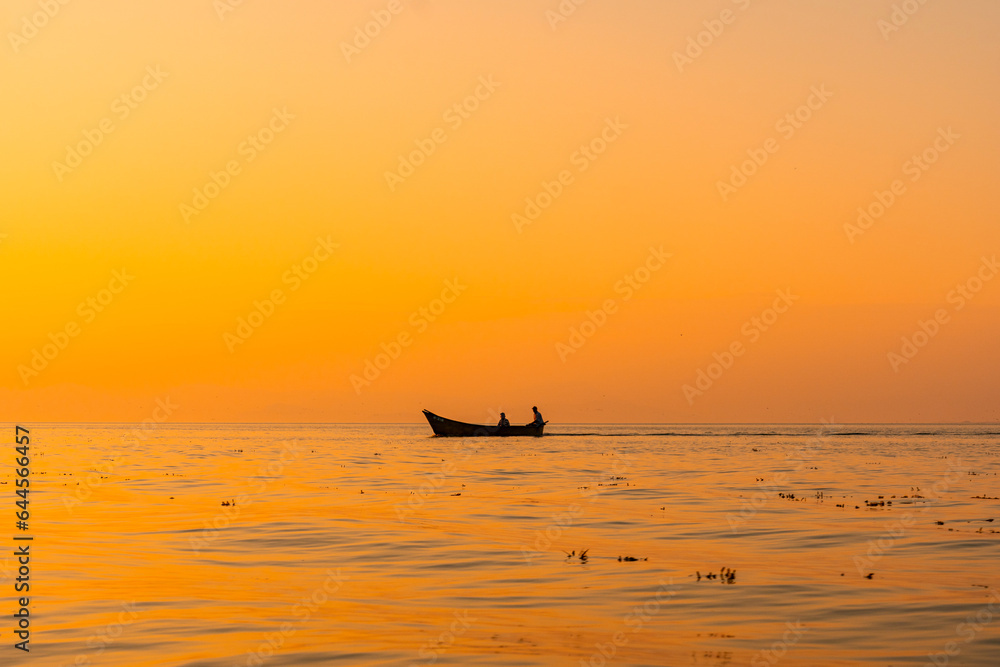 Fototapeta premium Fishing boat with a fisherman fishing in the orange sunset of Shkoder Lake in Shiroka. Albania