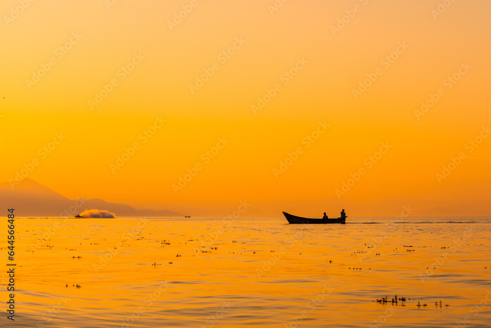 Fishing boat with a fisherman fishing in the orange sunset of Shkoder Lake in Shiroka. Albania