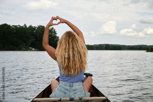 Mujer sentada en canoa en un lago haciendo un corazón con las manos