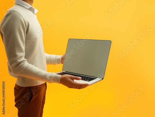 Man in causal clothing holding laptop in front of yellow background