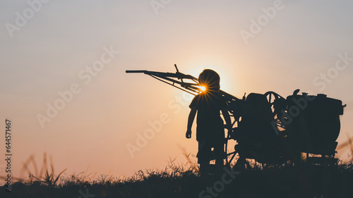 Silhouette of boy standing on field back plowing wagon, concept of agriculture and global kitchen in future.