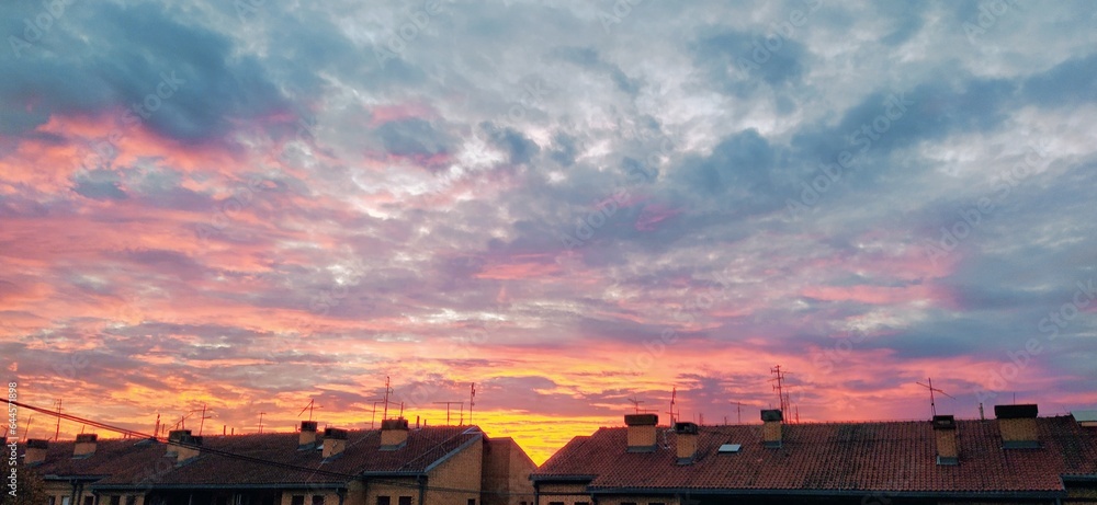 Dramatic beautiful clouds during sunset. Cumulus clouds illuminated in orange and pink. Dark and gray tones. Banner. Delicate pastel colors. Clouds over the rooftops of the city