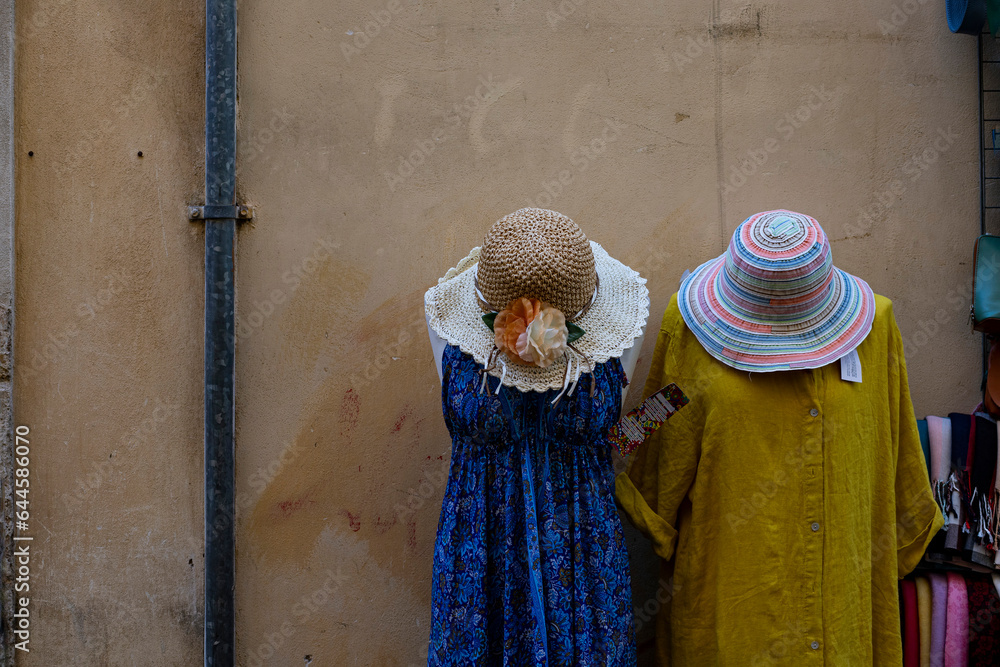 2 colorful dresses with straw hats hanging outside a quaint shop in Rome 2 colorful dresses with straw hats hanging outside a quaint shop in Rome