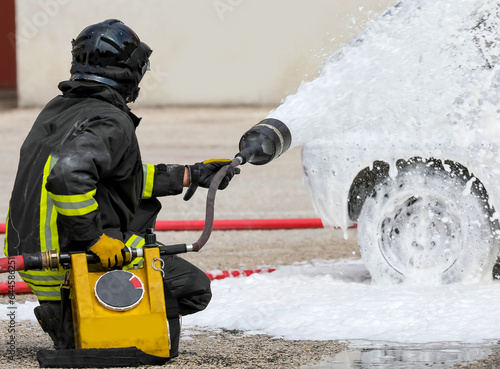 brave fireman extinguishing the fire of the car with foam after the traffic accident