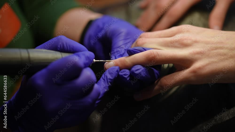 Closeup cutting cuticles on male fingers with nail drill machine in slow motion. Close-up unrecognizable professional beautician doing manicure for young Caucasian man in beauty salon indoors Closeup cutting cuticles on male fingers with nail drill machine in slow motion. Close-up unrecognizable professional beautician doing manicure for young Caucasian man in beauty salon indoors