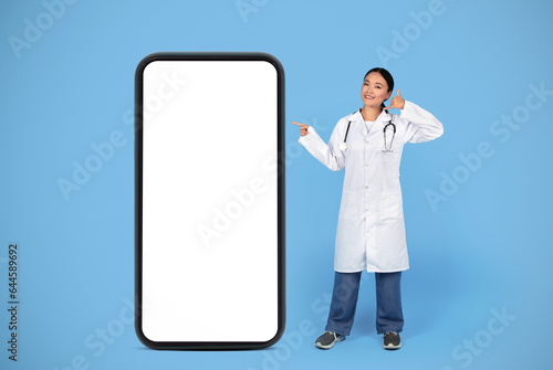 Smiling Asian Doctor Lady Gesturing Call Me While Standing Near Blank Smartphone
