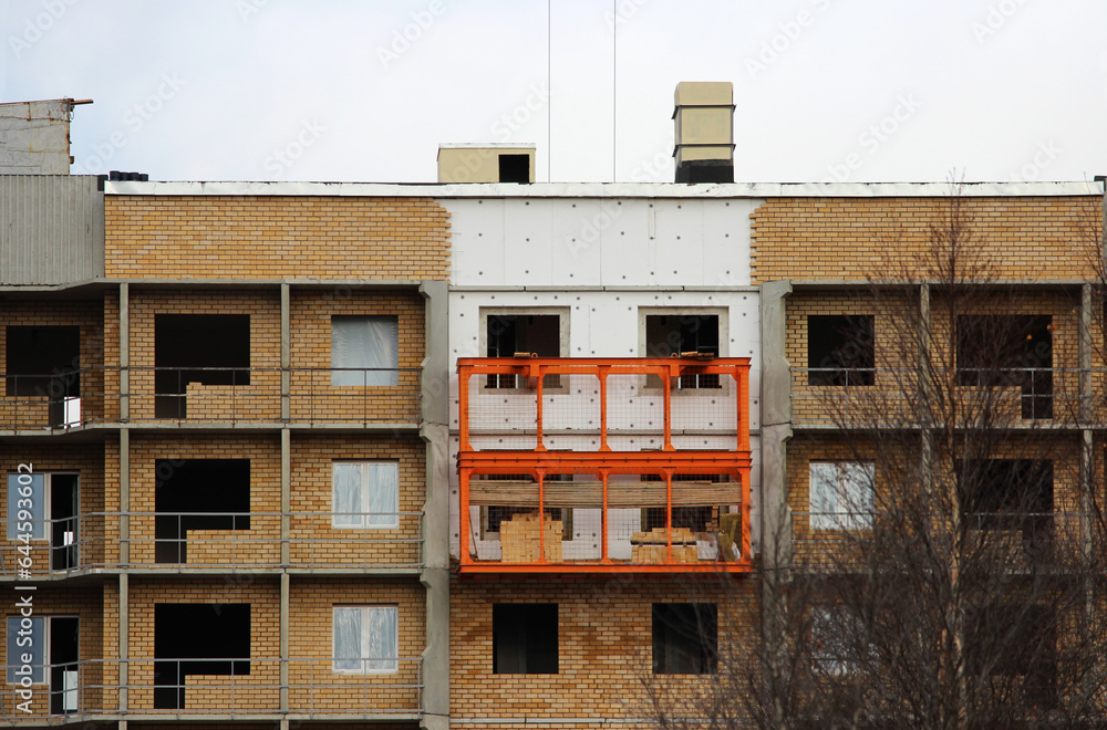 orange cradle against the background of a windowless brick house under construction. work at height or hazardous work or extreme house facade