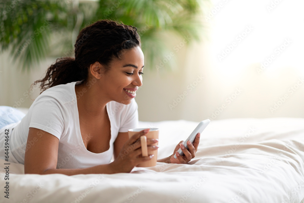 Nice App. Smiling Black Woman Using Smartphone And Drinking Coffee In Bed Nice App. Smiling Black Woman Using Smartphone And Drinking Coffee In Bed