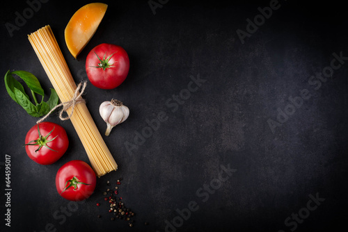 Spaghetti,tomatoes,cheese,basil,spices and garlic on a dark background with space for writing text.Cooking food concept.