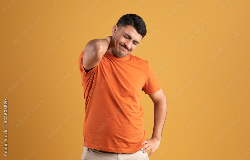 Sad brazilian man in t-shirt pressing his hand to neck and suffering from muscle pain, posing on yellow background Sad brazilian man in t-shirt pressing his hand to neck and suffering from muscle pain, posing on yellow background