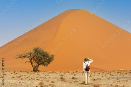 Young caucasic traveler standing  near orange sand dune with her hand on the hat. Travel desert concept photo