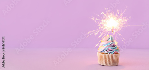 Tasty birthday cupcake with sparkler on lilac background with space for text