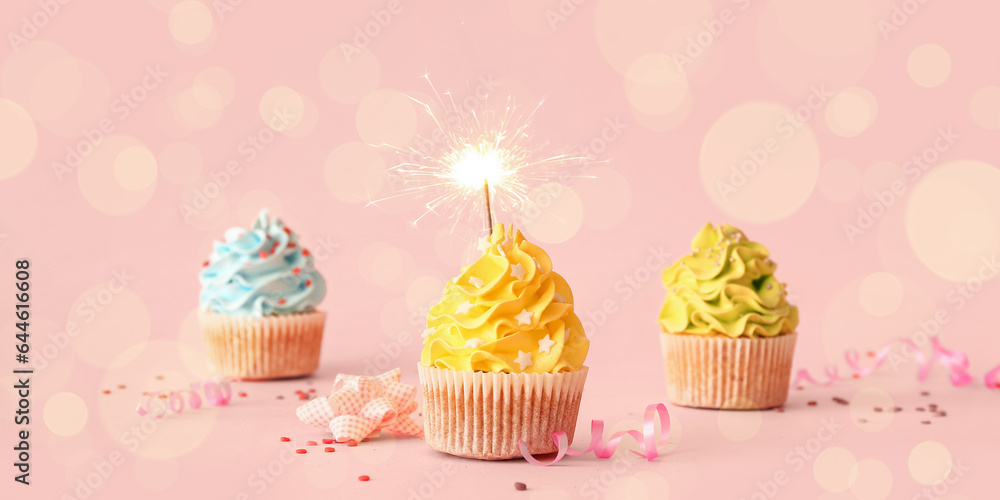 Tasty birthday cupcakes with sparkler and decor on pink background Tasty birthday cupcakes with sparkler and decor on pink background