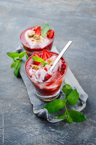 Traditional frozen strawberry soup with strawberry ice cream and crumbles served as a close-up on a grey stone design tray with text space photo