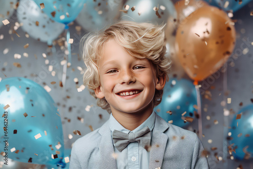 Happy beautiful toddler boy with blond hair, confetti around, cheerful happy kid portrait, happy birthday party balloons, blue white pastel colors. 