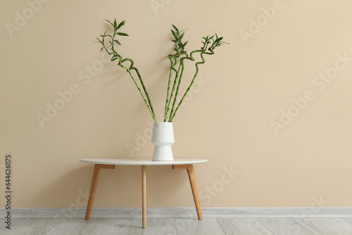Vase with bamboo stems on table near color wall
