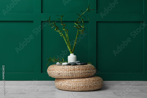 Vase with bamboo stems and stones on pouf against color background