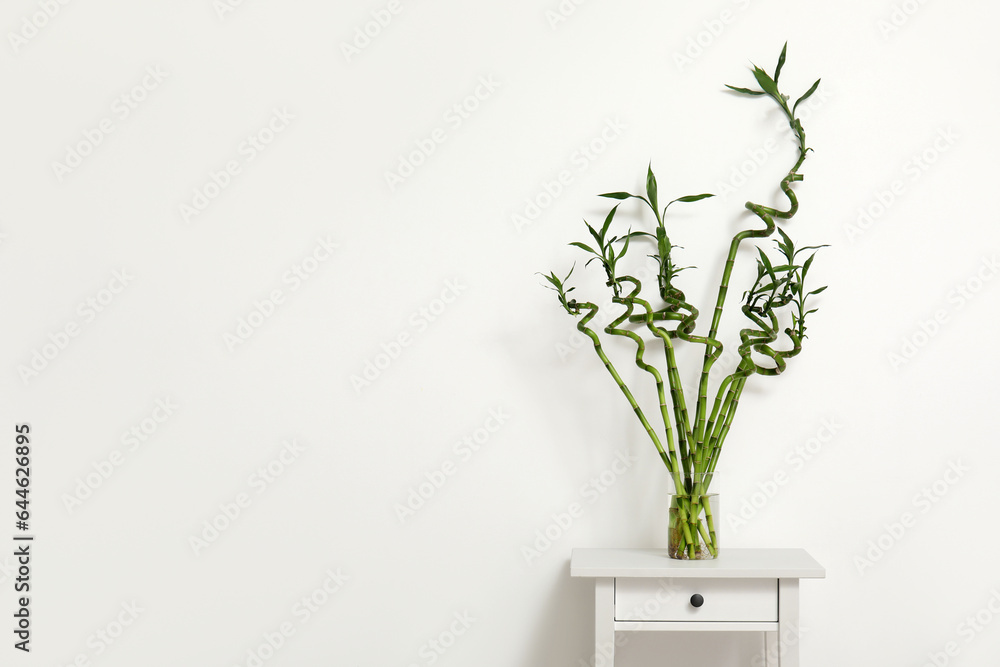 Vase with bamboo stems on table near light wall Vase with bamboo stems on table near light wall