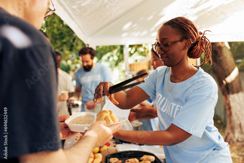 Detailed image of black woman at a food drive sharing free warm meals to poor caucasian homeless person. At local center group of volunteers feed and support the hungry and underprivileged.