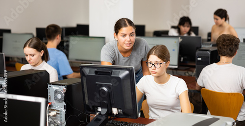 Schoolgirl using computer and teacher helping to him in classroom