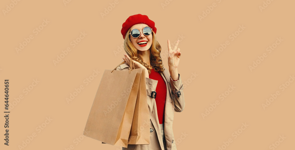 Autumn style outfit, portrait of beautiful happy smiling young woman with shopping bags wearing red french beret hat, gray coat jacket on beige studio background