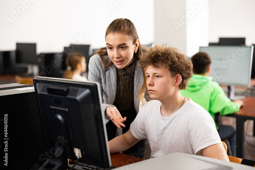 Teacher explaining task solution to teenage boy during computer science lesson in school. © JackF