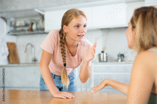 Teenage daughter enthusiastically happily tells unrecognizable mother about planned vacation with friends and classmates. Girl in focus