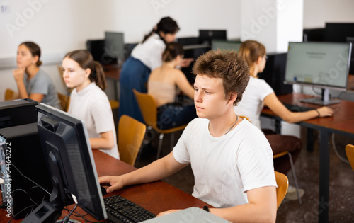 Teenage caucasian boy learning to use personal computer during lesson in school.