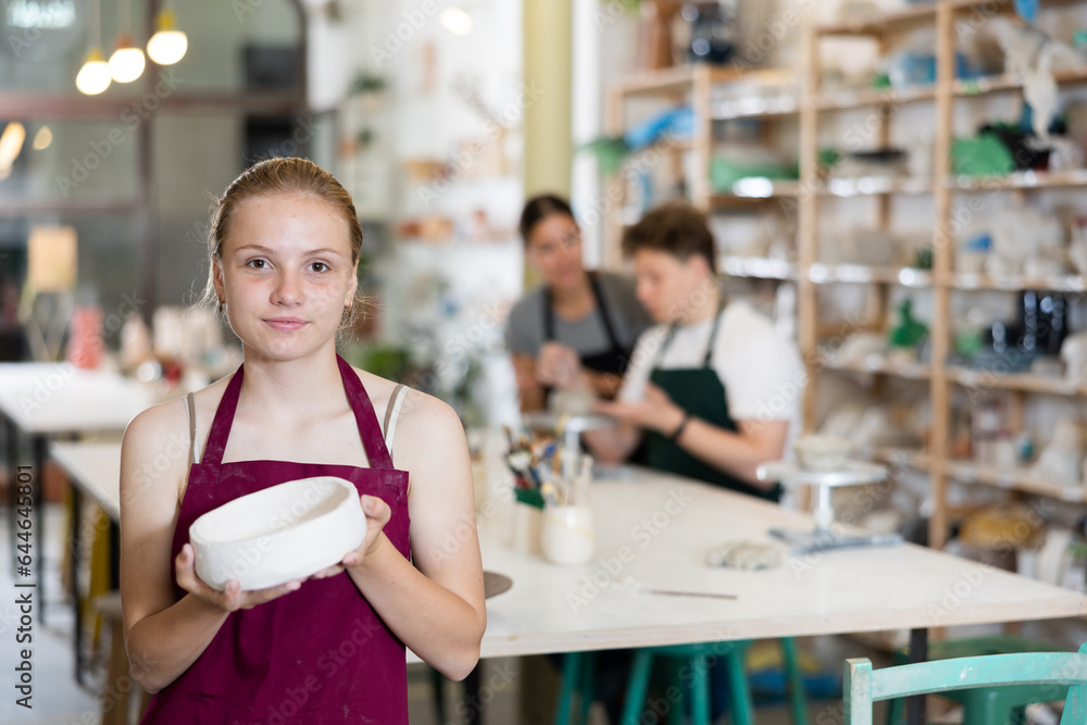 Satisfied teenager girl shows cup created by himself in a clay workshop